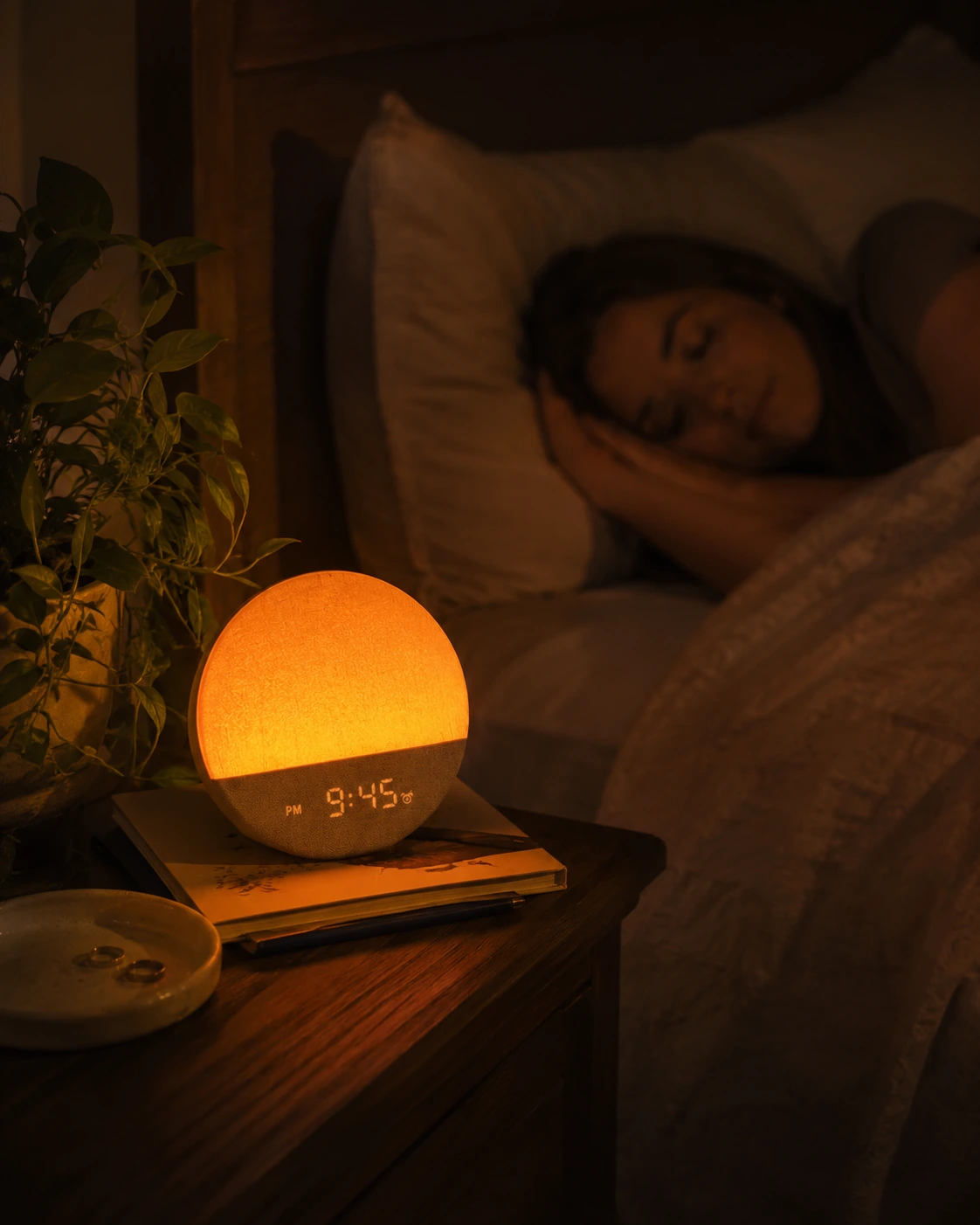 Dreamegg Sunrise 1 Wake Up Alarm Clock casting a warm orange glow on a bedside table while a person sleeps.